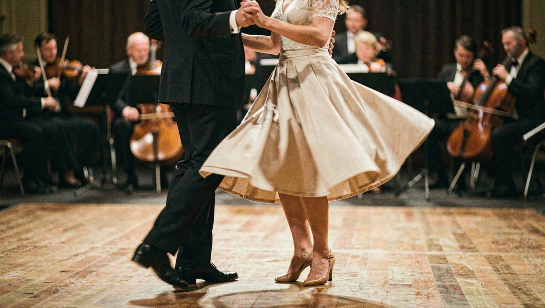Couple de danseurs de swing sur un plancher de bal en bois, jupe en mouvement, orchestre flou en arrière-plan, lumière chaude, cadrage vertical en pied